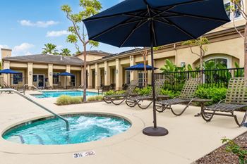 A pool with a blue umbrella and chairs around it.